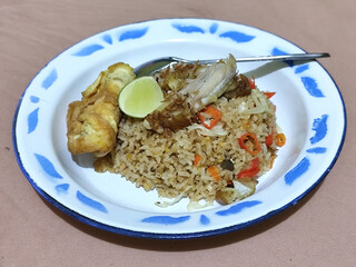 Fried rice with omelet, chicken pieces and red chili slices, has a delicious taste, served on a classic iron plate, with a brown background.