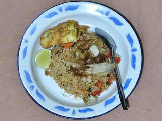 Fried rice with omelet, chicken pieces and red chili slices, has a delicious taste, served on a classic iron plate, with a brown background.