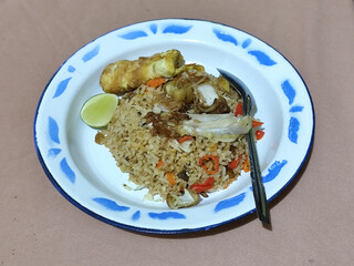 Fried rice with omelet, chicken pieces and red chili slices, has a delicious taste, served on a classic iron plate, with a brown background.