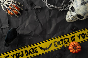 Halloween-themed still life featuring a skull, skeleton, pumpkins, caution tape, and spooky props