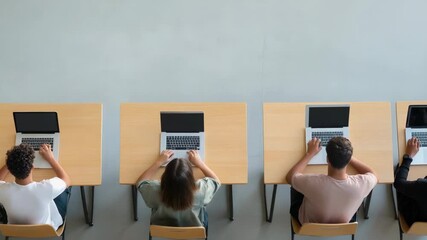 High school students are sitting at individual desks, using laptops with blank screens, possibly learning coding or taking a test, viewed from above in a modern classroom setting - Powered by Adobe