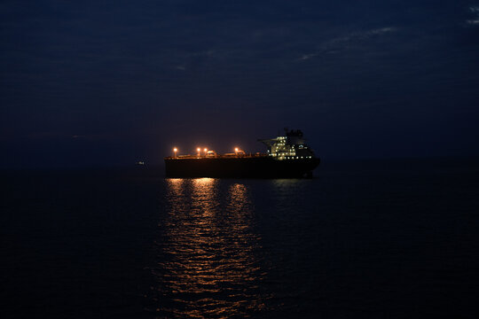 illuminated cargo ship sailing in the ocean at night under a starlit sky