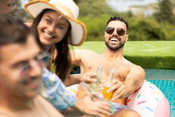 A joyful group of friends relaxing by the pool, enjoying drinks and happy moments in the sun on a warm summer day.