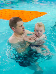 A man is holding a child in a pool.
