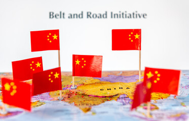 A Belt And Road Initiative concept with the Chinese national flags on various parts of a world map and the words belt and road initiative in the background.