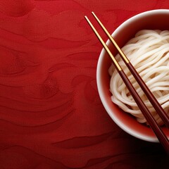 A bowl of plain white noodles with chopsticks resting on the edge, set against a textured red surface.