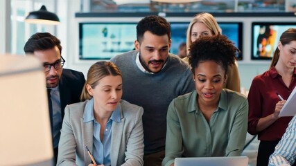 A diverse team collaborates intensely around a laptop, reviewing data on screens in a modern office. - Powered by Adobe