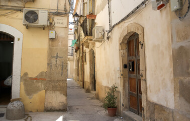 Narrow cobblestone alleyway in historic town with rustic buildings and potted plants creating...