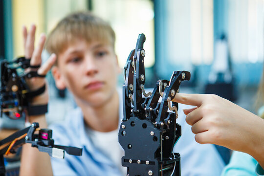 Teenage student testing robotic hand in classroom during STEM education project, focusing on interaction between human and robotic technology.