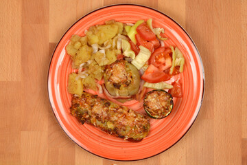 A colorful plate features stuffed vegetables with lentils, potato salad, and a fresh tomato and pepper salad