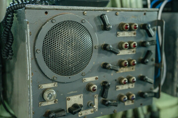 Close-up of a vintage military speaker unit with multiple labeled switches, knobs, and signal...