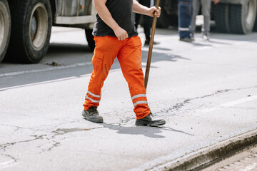 Construction worker in orange pants repairing a city road during the daytime with ongoing traffic nearby