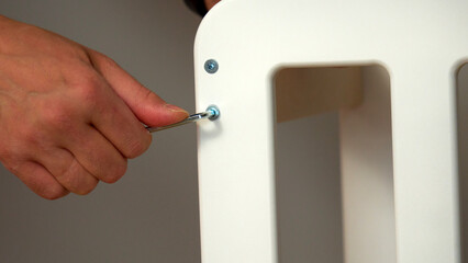 A hand grips a wrench as it tightens a bolt on a white furniture piece