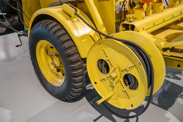 This detailed image shows the large rubber tire and circular cable reel of a yellow utility...