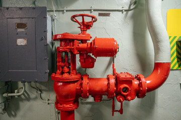 Bright red mechanical valve system with a large control wheel, set against a light green wall on a...