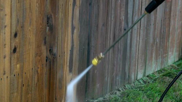Pressure washer cleaning a weathered wooden fence outdoors