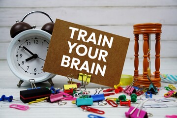 Train Your Brain text on paper card with alarm clock and stationary on wooden background