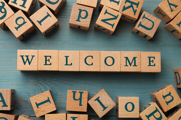 Word Welcome made of wooden cubes on light blue table, flat lay