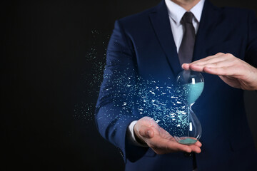Time running out. Hourglass dissolving in man's hands against black background, closeup