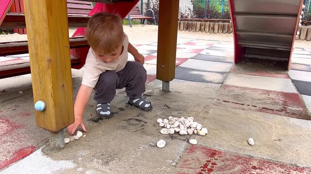 Little boy playing with pebbles at a playground, throwing stones