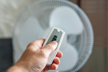 Man using remote control to turn on or off floor fan in room
