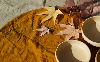 A cozy autumn scene featuring maple leaves, ceramic bowls, and glware arranged on a textured yellow tablecloth