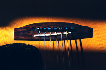 Acoustic guitar bridge and strings. Wooden guitar bridge, with strings and tuning pegs in sharp...
