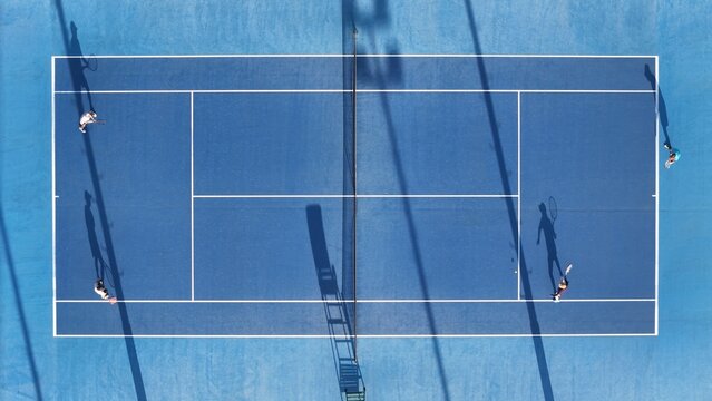 Aerial View of Blue Tennis Courts with Players and Shadows