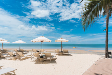 Beachfront lounge chairs with parasol facing tropical sea on sunny day