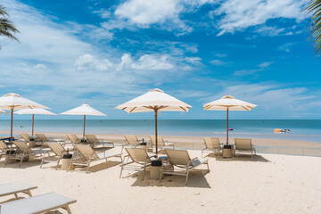 Beachfront lounge chairs with parasol facing tropical sea on sunny day
