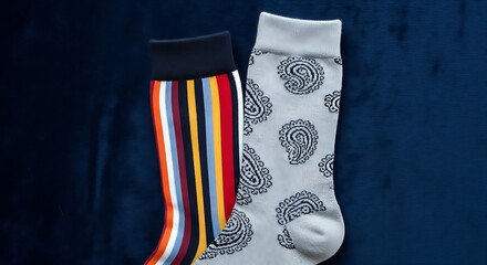 Two socks, one with colorful vertical stripes and the other with a paisley pattern, are displayed against a dark blue background.