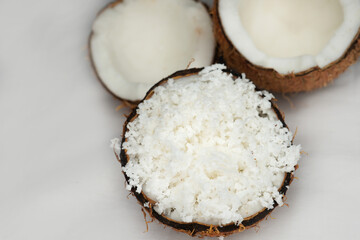 Freshly grated coconut pulp in cracked coconut shell and half of split coconut on white background. File contains clipping path.