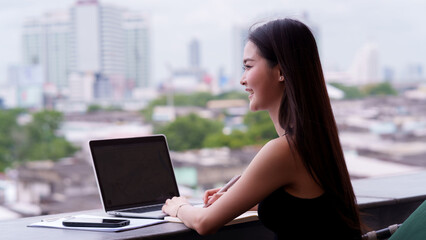 Asian adult professional woman working on laptop computer writing notes outdoors urban city setting modern confident remote business entrepreneur