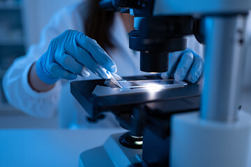 Photo of a scientist in blue gloves carefully places a slide under a microscope