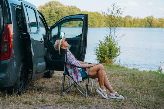 Woman sits peacefully beside her campervan at a quiet lakeside spot, surrounded by nature.