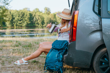 A woman relaxes in nature beside a Mini Camper by the lake enjoying vanlife freedom and a peaceful solo outdoor moment