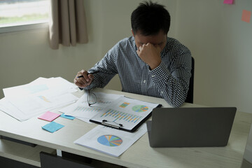 An asian business male manager is working with paper documents and laptop in office and suffering from headache and depression during working, employee life office stress and office syndrome concept.