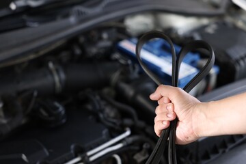 Obraz premium Auto mechanic with timing belt near open hood of car indoors, closeup. Space for text