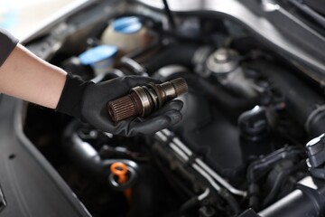 Auto part. Professional mechanic with drive shaft near open hood of car indoors, closeup. Space for text