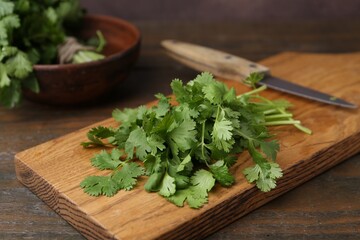 Cutting board with fresh cilantro and knife on wooden table, closeup