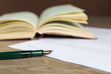 Notary document and fountain pen on wooden table against brown background, selective focus
