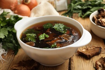 Tasty soup with mushrooms and parsley in bowl on wooden table, closeup
