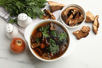 Tasty soup with mushrooms and parsley in bowl on white marble table, flat lay