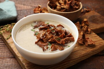 Tasty cream soup with mushrooms and thyme in bowl on wooden table, closeup