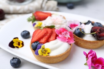 Sweet tartlets with berries and flowers on light table, closeup. Delicious dessert