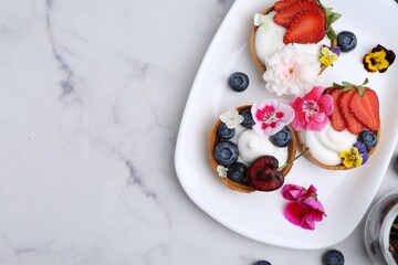 Sweet tartlets with berries and flowers on light marble table, flat lay with space for text. Delicious dessert