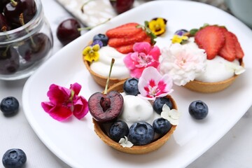 Sweet tartlets with berries and flowers on light table, closeup. Delicious dessert
