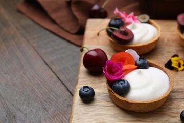 Sweet tartlets with berries and flowers on wooden table, closeup. Delicious dessert