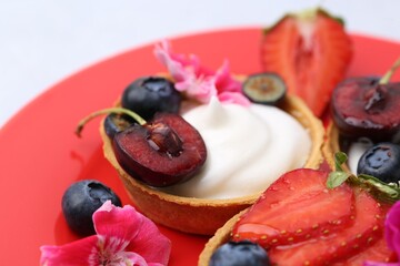 Sweet tartlets with berries and flowers on red plate against light background, closeup. Delicious dessert