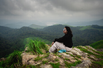 Fototapeta premium Indian woman resting at a windy forest trek viewpoint in Vagamon, Idukki, Kerala